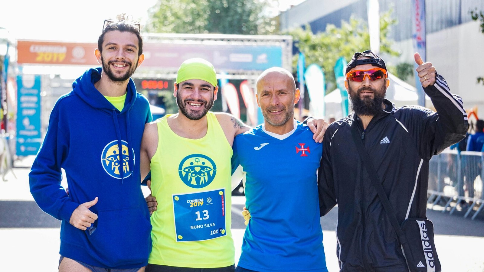 Four male marathon runners celebrating after a race, smiling and posing for the camera outdoors.