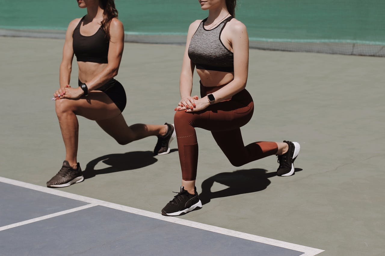 Two women doing lunges on a sports court, showcasing fitness and workout fashion.